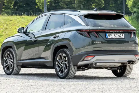 Tylna część ciemnozielonego Hyundaia Tucsona hybrydowego na żwirowej drodze. Wiele osób szuka hyundai tucson opinie przed zakupem.