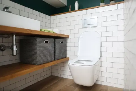 Nowa deska wolnoopadająca do toalety. W łazience białe kafelki, drewniane półki z koszami i nowoczesna miska WC.