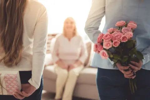 Dwie córki ukrywają prezent i bukiet róż dla mamy z okazji dnia matki.