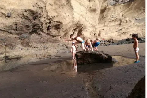 Un grupo de niños exploran una poza en la playa, rodeados de acantilados rocosos.