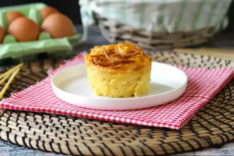 En gyllene, krispig makaronipudding på en vit tallrik, perfekt för ett maskros recept. Ägg i bakgrunden.
