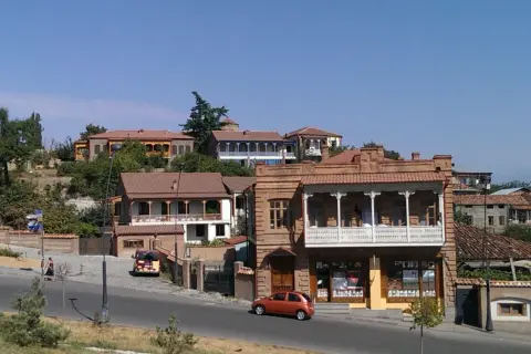 Urokliwe uliczki Telavi, Gruzja, z tradycyjną architekturą i balkonami. Pomarańczowy samochód jedzie po drodze.
