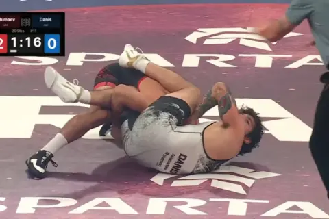 Intens kamp i catch wrestling. En brottare har den andra i ett grepp på mattan.
