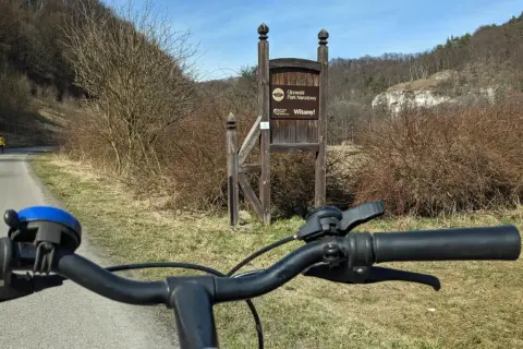 Rowerem przez Ojcowski Park Narodowy. Wita nas drewniany drogowskaz i malownicze wapienne skały w tle.