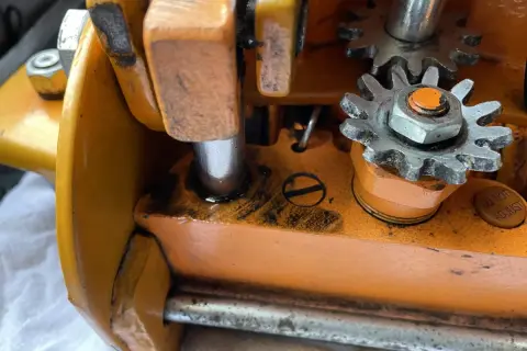 Zbliżenie na mechanizm zębatkowy pomarańczowego lewarka z widocznymi śladami oleju.