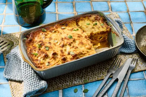 Herzhafte Moussaka mit Zucchini, goldbraun gebacken, wartet darauf, serviert zu werden. Ein Stück ist bereits auf einem Teller angerichtet.