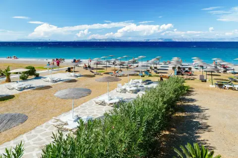 Słoneczna plaża Faliraki by Sun Palace z leżakami i parasolami. Turkusowe morze i góry w tle.