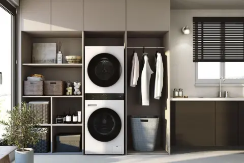 Ein moderner Waschraum mit einem Trockner, der auf einer Waschmaschine steht. Daneben hängen Kleider und ein Wäschekorb.