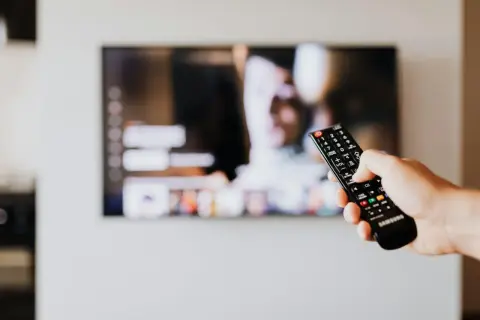 Dłoń trzyma pilot Samsunga, celując w ekran telewizora. Chcesz wiedzieć, jak wyłączyć audiodeskrypcję Samsung?