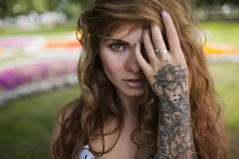 Frau mit welligem Haar und einem detaillierten Mandala Handgelenk Tattoo, das sich über ihren Unterarm erstreckt.