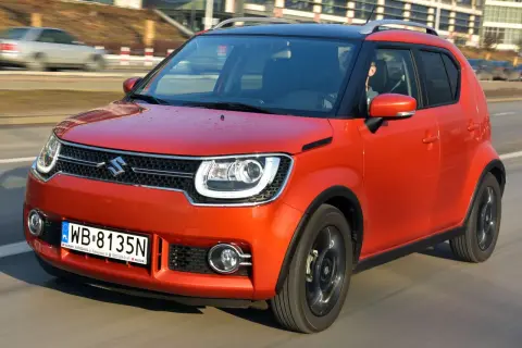 Pomarańczowy Suzuki Ignis z czarnym dachem pędzi po drodze. Kierowca w środku.