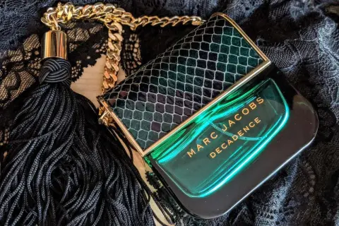 Flakon perfum Marc Jacobs Decadence w zielonym, wężowym wzorze, z czarnym frędzlem i złotym łańcuszkiem, emanuje luksusem.