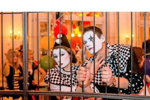 Zwei Clowns hinter Gittern, bereit für den Dresden Karneval. Bunte Ballons und Lichter im Hintergrund.