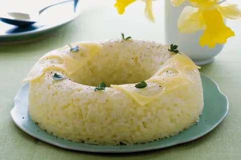 Sformato di riso a ciambella, decorato con fette di formaggio e prezzemolo, su un piatto verde.