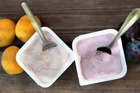 Dwa kubeczki jogurtu, jeden z brzoskwiniami, drugi ze śliwkami, kuszą by sprawdzić, czy można jeść zważony jogurt.