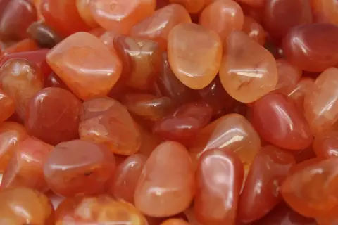 Tanti sassolini levigati di agata marrone, con sfumature arancioni e rosse, noti per le loro proprietà energizzanti.