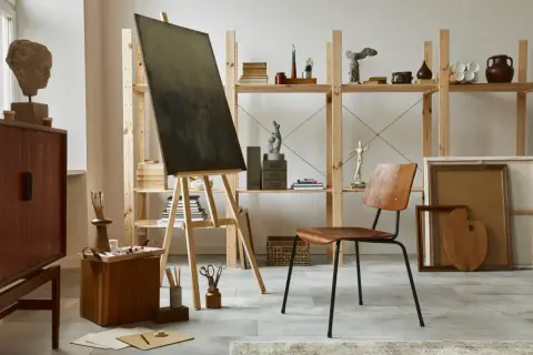 An art studio aesthetic with a canvas on an easel, wooden furniture, sculptures, and art supplies.