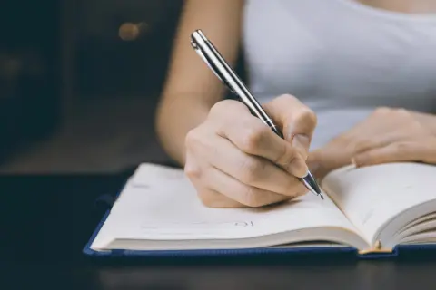 Dłoń pisząca długopisem w otwartym notatniku.