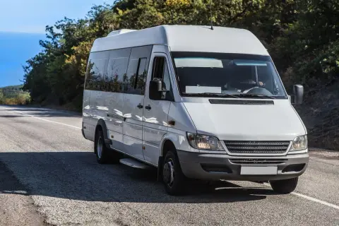 Weißer Kleinbus von Polen nach Deutschland fährt auf einer Straße durch eine hügelige Landschaft.
