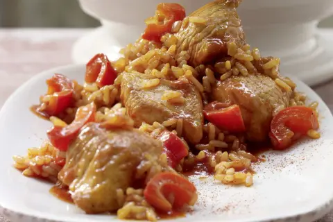 Serbisches Reisfleisch mit zarten Fleischstücken und roten Tomaten, serviert auf einem weißen Teller.