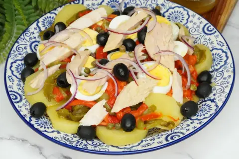 Deliciosa ensalada de patata con atún, huevo duro, pimientos asados, aceitunas negras y cebolla morada.