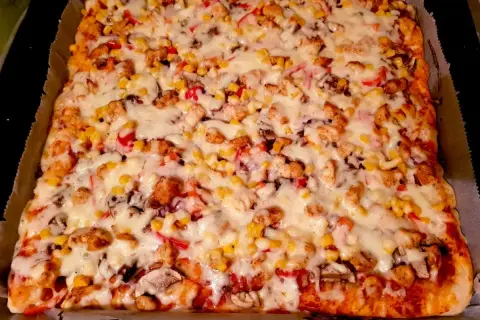 Pyszna pizza domowa na blachę z kurczakiem, kukurydzą i pieczarkami, obficie posypana serem. Idealna na rodzinny obiad.