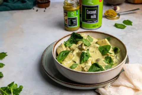 Miseczka zielonego curry z kurczakiem i szpinakiem, obok puszka mleka kokosowego i słoiczek pasty curry.