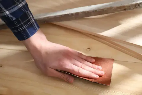 Mano lijando madera con lija, preparando la superficie para un acabado perfecto.