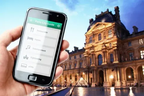 Smartfon z przewodnikiem po Paryżu w dłoni, w tle Luwr. Odkrywaj kody Francji!