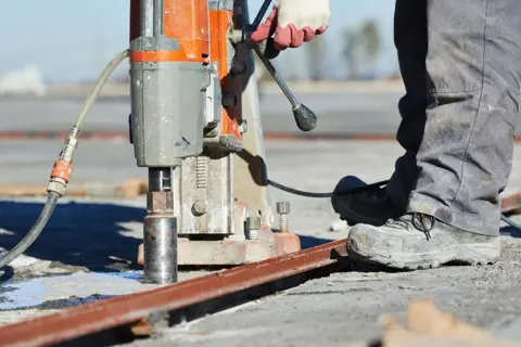Robotnik wykonuje wiercenie dużych otworów w metalu za pomocą wiertnicy rdzeniowej.