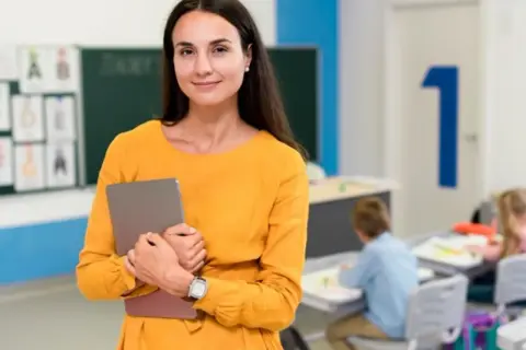 Nauczycielka z tabletem w klasie, przygotowująca się do zajęć, które mogą być częścią studiów podyplomowych nauczyciel wspomagający.