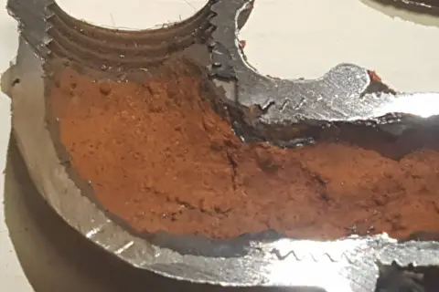 Sezione di tubo metallico con incrostazioni marroni che mostrano come evitare la formazione di calcare nelle tubazioni.
