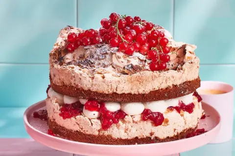 Ein zweistöckiger Johannisbeer Baiser Kuchen mit Schokoladenböden, Sahne und roten Johannisbeeren.