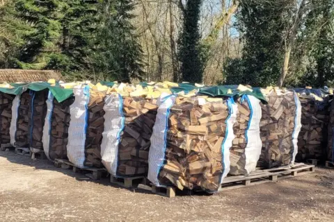 Reihenweise Säcke mit gespaltenem Brennholz, bereit zum Trocknen. Die Frage "wie lange holz trocknen" beschäftigt jeden, der diesen Anblick sieht.