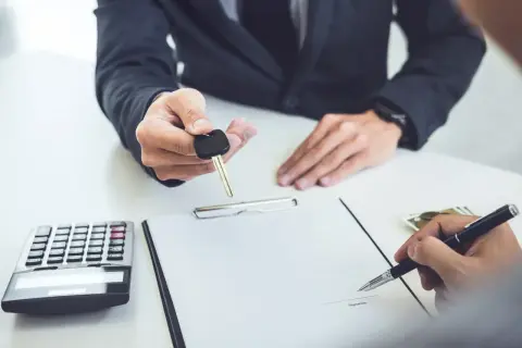Przekazanie kluczyków do samochodu po podpisaniu umowy leasingu finansowego. Obok kalkulator i pieniądze.