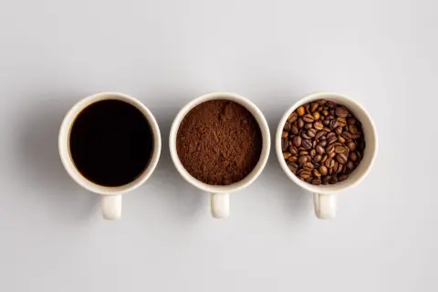 Tre tazze mostrano il viaggio del caffè: chicchi tostati, macinato e bevanda scura. Un'idea di da dove proviene il caffè.