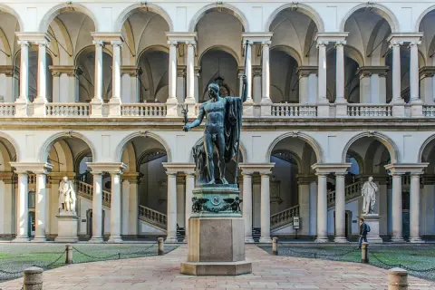 Dziedziniec Pinacoteca di Brera z rzeźbą w centrum i arkadowymi galeriami.