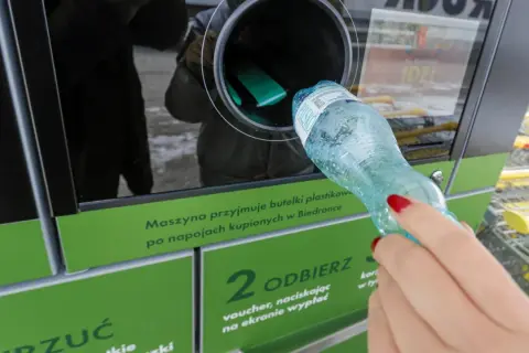 Kobieta wrzuca plastikową butelkę do maszyny przyjmującej opakowania.