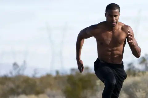 Uomo a torso nudo corre, mostrando i suoi addominali scolpiti. La corsa coinvolge potenti muscoli delle gambe e del core.