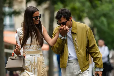 Ein Mann küsst die Hand einer Frau. Sein Outfit für ein erstes Date: gelbe Jacke, weißes T-Shirt, helle Hose. Sie trägt ein gemustertes Kleid und eine Tasche.