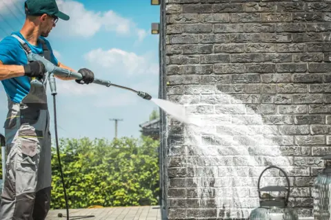 Mann reinigt Klinkerwand mit Hochdruckreiniger.