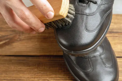 Brosse en bois appliquant un produit sur une chaussure en cuir noir. Pour imperméabiliser chaussures avant ou après cirage, un bon entretien est essentiel.