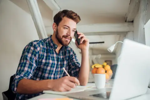 Mężczyzna rozmawia przez telefon, notuje i pracuje przy laptopie. To dobry moment, by zastanowić się, kiedy najlepiej szukać pracy.