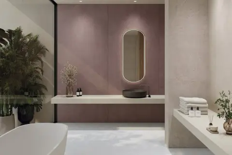 Elegante baño moderno con lavabo de piedra, espejo ovalado iluminado y azulejos de pared en tono malva. Toallas apiladas y plantas aportan calidez.