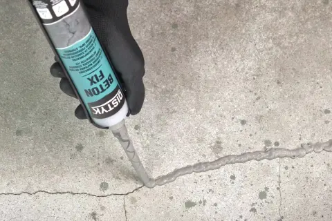 Ręka w czarnej rękawiczce aplikuje masę Distyk Beton Fix na pęknięcie w betonie, pokazując, jak połączyć stary beton z nowym.