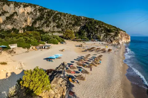 Piękna plaża w Albanii, morze lśni w słońcu, a klif tworzy malownicze tło dla leżaków i parasoli.