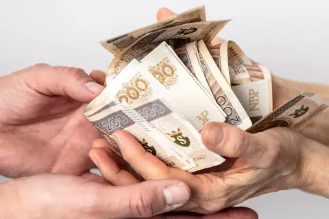 Dwie pary rąk przekazują sobie plik banknotów 200 zł. Może to być darowizna, od której należy zapłacić podatek od darowizny.