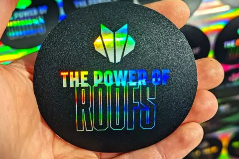 Okrągły czarny naklejka z holograficznym logo i napisem "THE POWER OF ROOFS".