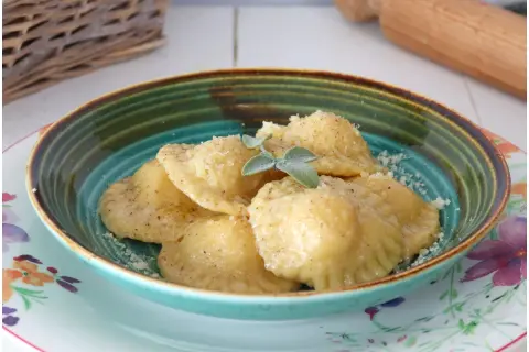 Tortelli di patate fumanti, cosparsi di parmigiano e guarniti con salvia, in una ciotola colorata.