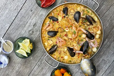 Ein köstliches Paella-Rezept mit Garnelen, Muscheln und Reis, garniert mit Zitronenspalten und Paprika.